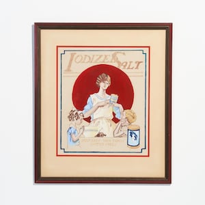 May include: A vintage framed advertisement for Iodized Salt. The ad features a woman in a blue dress and apron, with two children, holding a box of salt. The text reads "Help Keep Your Family Goiter Free!"
