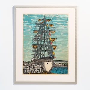 May include: Framed print of a tall ship with sails and flags. The artwork shows the ship at a pier with figures on the shore. The sky is blue with textured brushstrokes, and the frame is silver. The artwork is in a silver frame.