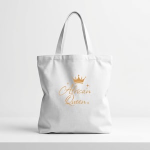 Puede incluir: Bolso tote blanco con una corona dorada y las palabras "African Queen" en una escritura elegante. El bolso tiene un diseño sencillo con asas largas para llevarlo al hombro.
