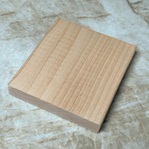 May include: A rectangular, light-colored wooden block with visible wood grain. The block has a smooth, sanded surface and a natural, unfinished appearance. The edges are cleanly cut, suggesting a craft or woodworking project.