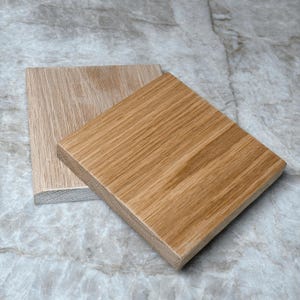 May include: Two square wooden planks with visible wood grain. One plank is a light tan color, and the other is a medium brown. The planks are positioned at an angle, showcasing the natural wood texture and color variations.