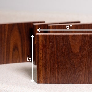 May include: Four wooden coasters in a dark brown wood grain finish. The coasters are 5 inches tall and 6 inches wide.