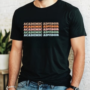 May include: Black t-shirt with the text "ACADEMIC ADVISOR" in a stacked, retro-style design. The text is in a gradient of colors, including orange, pink, and blue. The shirt is a crew neck style.