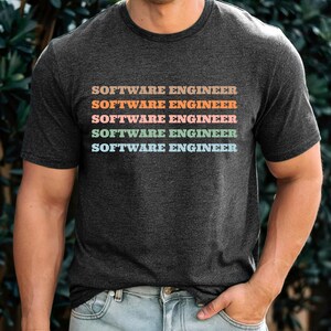 Peut inclure: Un t-shirt gris chiné foncé avec le texte "SOFTWARE ENGINEER" répété cinq fois dans différentes couleurs pastel.
