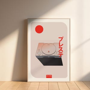 以下が含まれることがあります： PlayStationコンソールのスタイリッシュなイラストが描かれたフレーム入りアートプリント。赤い円と日本語のテキストが特徴のミニマリストデザイン。コンソールはグレーと黒の色合いで表現され、淡いピンク色の背景に配置されています。