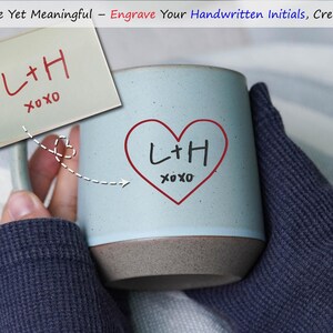May include: A light blue ceramic mug with a brown base, featuring a red heart with the initials "L+H" and "xoxo" written inside. A sticky note with the same initials and text is held next to the mug. The text "Simple Yet Meaningful" is at the top.