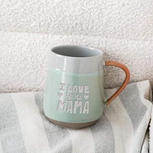 May include: A white ceramic mug with a black handle and the text "But First, Coffee" in a bold, black font. The mug is set against a neutral background, highlighting its simple design.