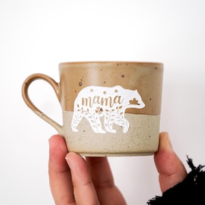 May include: A brown ceramic mug with a white bear design and the word "mama" on it.
