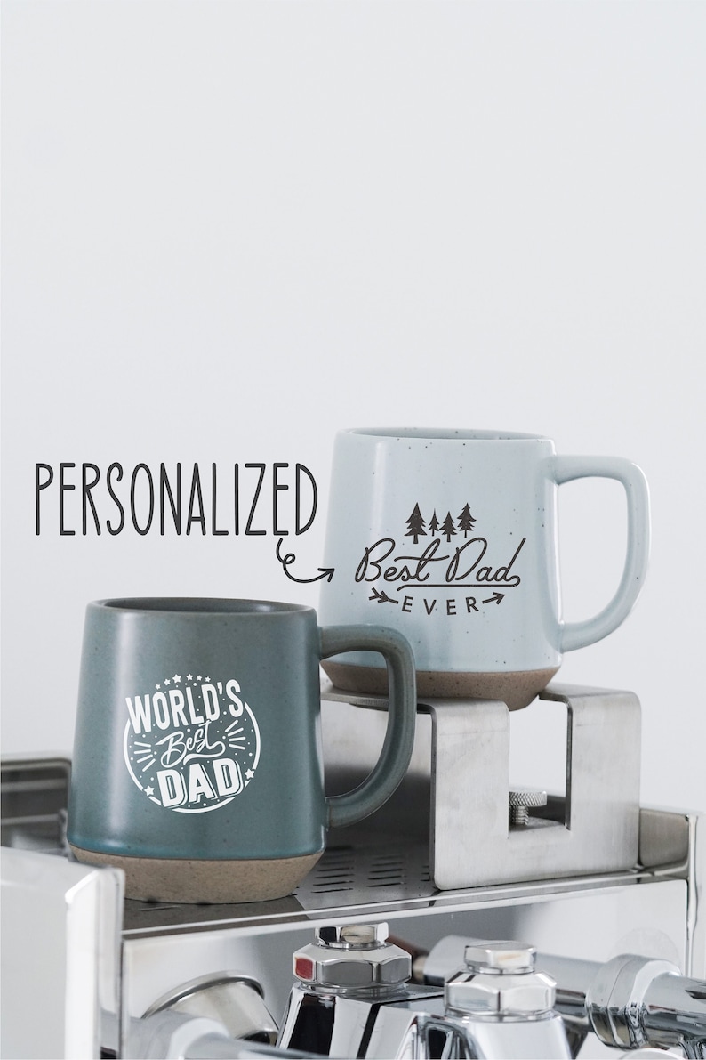 May include: Two ceramic mugs with the text "World's Best Dad" and "Best Dad Ever". The mugs are teal and light blue with brown bases. The word "Personalized" is written in the image.