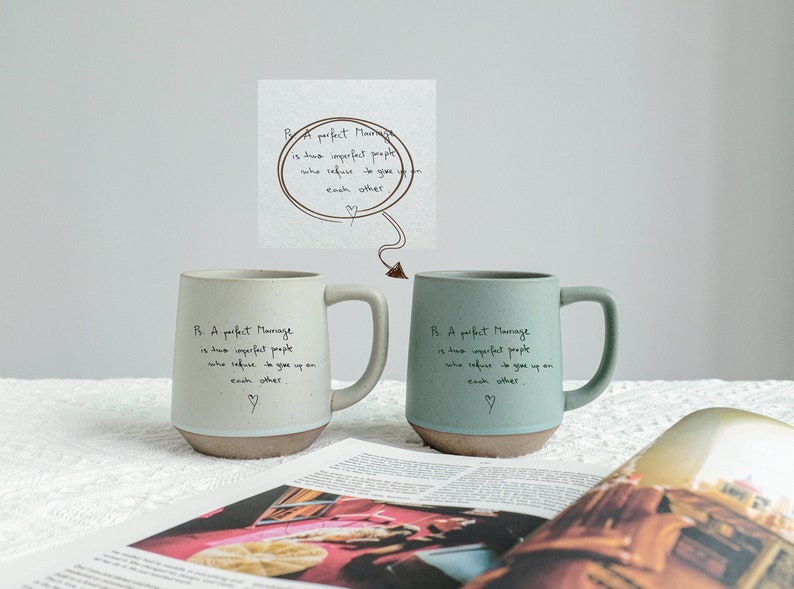 May include: Two ceramic mugs, one light green and one teal, with a brown base and handle. Each mug has the text "A perfect marriage is two imperfect people who refuse to give up on each other." A small illustration is above the mugs.