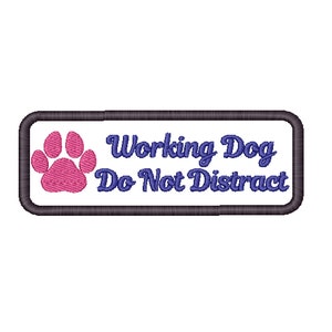 May include: A white rectangular patch with a black border. The patch has a pink paw print and the text "Working Dog Do Not Distract" in blue.