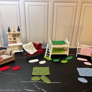 May include: Miniature dollhouse furniture set including a beige sofa with a red crocheted blanket, a red loveseat with a white crocheted blanket, and a white bunk bed with a green crocheted blanket. Also includes crocheted rugs.