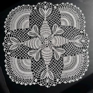 May include: A white, square doily with an intricate crochet design. The doily features a central floral motif surrounded by symmetrical fan-shaped patterns and delicate openwork. The detailed craftsmanship creates a lace-like appearance, perfect for home decor.