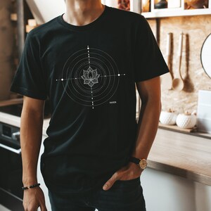 Pode incluir: Uma camiseta preta com um design geom&eacute;trico branco que apresenta uma flor de l&oacute;tus no centro. O design &eacute; cercado por c&iacute;rculos conc&ecirc;ntricos e pontos.
