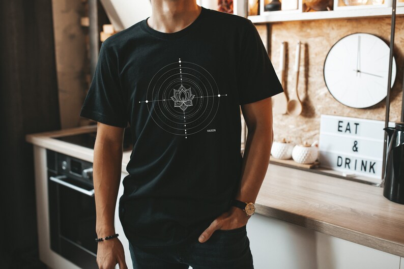 Pode incluir: Uma camiseta preta com um design geom&eacute;trico branco que apresenta uma flor de l&oacute;tus no centro. O design &eacute; cercado por c&iacute;rculos conc&ecirc;ntricos e pontos.
