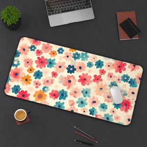 May include: A large desk mat with a floral pattern in shades of pink, red, blue, and yellow. The mat is on a black surface with a laptop, a cup of coffee, and a computer mouse.
