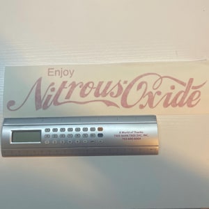 Puede incluir: Una pegatina blanca con el texto "Enjoy Nitrous Oxide" en letras rosas en cursiva.