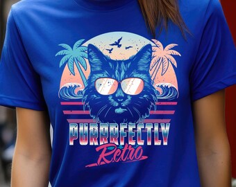 May include: Blue t-shirt featuring a retro design with a cat wearing sunglasses. The graphic includes palm trees, waves, and the text "PURRRFECTLY Retro" in a stylized font, evoking a vintage aesthetic.