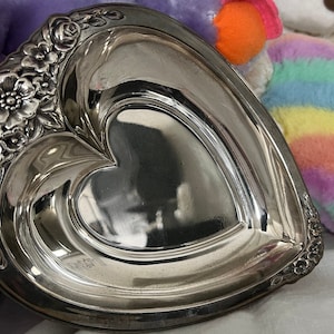 May include: A silver heart-shaped dish with a raised floral design around the edge.