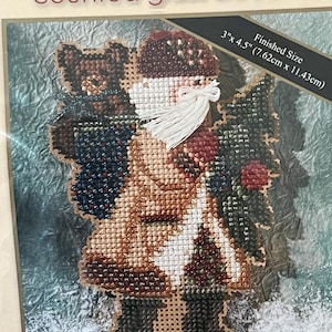 May include: A counted glass bead kit featuring a cross-stitch design of a Santa Claus figure carrying a teddy bear and a Christmas tree. The finished size is 3" x 4.5" (7.62cm x 11.43cm). The kit includes the text "counted glass bead kit".