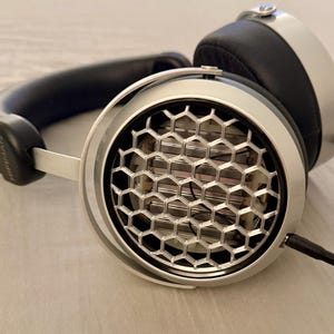 May include: Silver headphones with a honeycomb-shaped speaker grille. The headphones have a black headband and earcups.