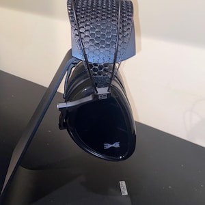 Puede incluir: Auriculares negros con un soporte negro. Los auriculares tienen un dise&ntilde;o de malla negra en la diadema y la palabra "Noble" es visible en la almohadilla.