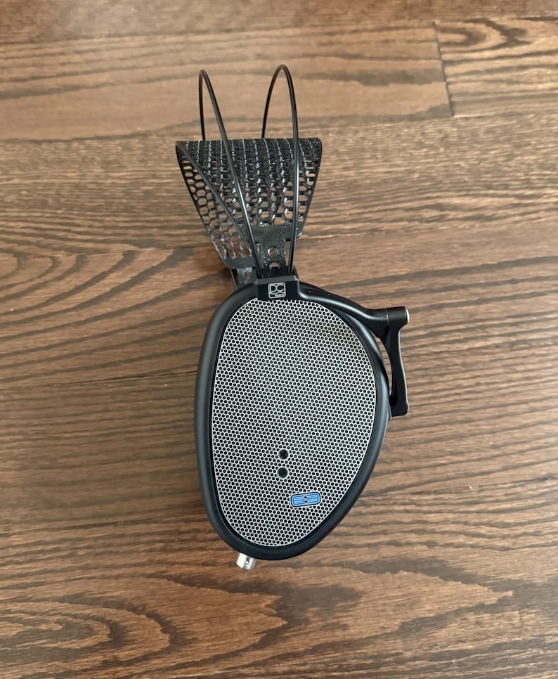 Puede incluir: Auriculares negros con diadema de malla y rejilla de altavoz plateada. Los auriculares tienen un logotipo azul en la rejilla del altavoz.