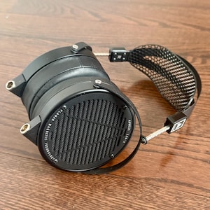 Op de afbeelding: Zwarte planaire magnetische hoofdtelefoon met een zwarte hoofdband en zwarte oorschelpen. De oorschelpen hebben een zwart metalen rooster en de tekst "Audeze LCD-X Planar Magnetic Technology" staat aan de zijkant gedrukt.