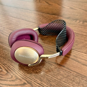 Può includere: Cuffie wireless color borgogna e oro con fascia in rete nera. Le cuffie hanno la scritta "Bowers & Wilkins" sul lato.
