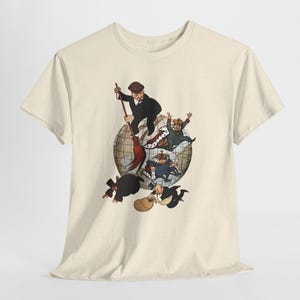 May include: A cream-coloured t-shirt with a cartoon illustration of a man sweeping figures off a globe with a broom. The figures are dressed in suits and crowns. The graphic is in shades of brown, black, red, and blue.