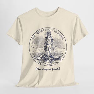 May include: Cream-colored t-shirt featuring a circular graphic with a classical illustration. The graphic depicts a figure standing over a fallen person, with the text "SIC SEMPER TYRANNIS" and "[Thus always to tyrants.]" printed in navy blue.