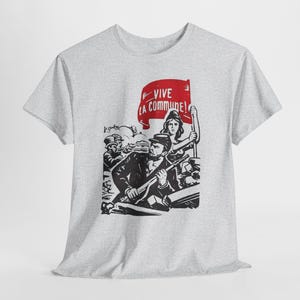 May include: A light grey short-sleeve t-shirt featuring a black and white graphic print of a historical scene with a person holding a rifle and another person holding a red flag with the text VIVE LA COMMUNE printed in white letters.