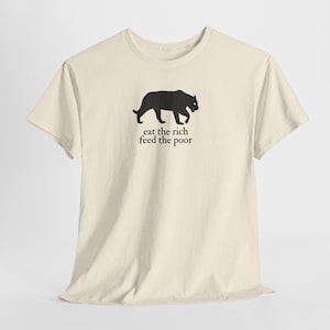 May include: Cream-colored t-shirt featuring a black panther silhouette above the text "eat the rich feed the poor". The shirt has a classic crew neck and short sleeves, suitable for casual wear.