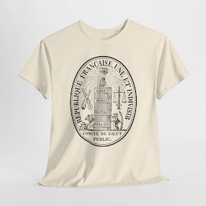 May include: A cream-coloured short-sleeve t-shirt featuring a black circular graphic print. The design includes the text REPUBLIQUE FRANCAISE, UNE ET INDIVISIB and COMITE DE SALUT PUBLIC, surrounding a central fasces with the words LIBERTE EGALITE FRATERNITE OU LA MORT.