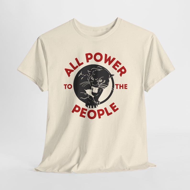 Cream-colored t-shirt featuring a black panther illustration inside a black circle. The text "ALL POWER TO THE PEOPLE" is printed in red around the circle. The shirt has short sleeves and a crew neck.