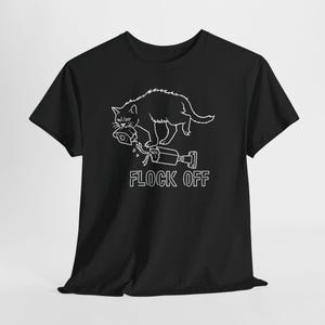 May include: A black short-sleeve t-shirt featuring a white line art graphic of a cat holding a broken security camera in its mouth. Below the cat, another broken security camera is depicted with the text FLOCK OFF in white lettering.