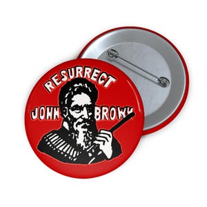 May include: A round pin-back button with a bright red background. The design features a black and white graphic of a bearded man holding a long object, with the text RESURRECT JOHN BROWN printed in white letters with a black outline.