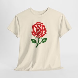 May include: A cream-coloured short-sleeve t-shirt featuring a graphic of a red rose on the chest. The letters DSA are integrated into the centre of the red rose petals. The rose has a green stem with two green leaves extending from the base.