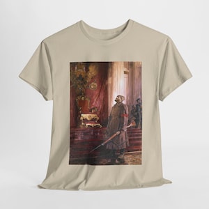 May include: A tan t-shirt featuring a historical painting of a man in a long coat holding a rifle. The painting depicts a scene with a throne, columns, and other figures. The artwork is in a classical style, with rich colors and detailed brushwork.