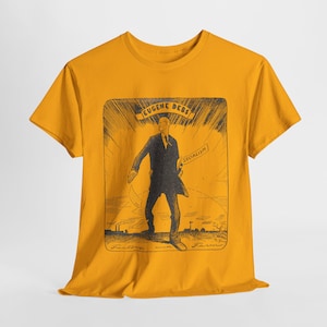 May include: Mustard yellow t-shirt featuring a black and white illustration of Eugene Debs. The graphic includes the text "EUGENE DEBS" above the figure and "SOCIALISM" on a banner. The bottom of the graphic reads "Factory and Farm".