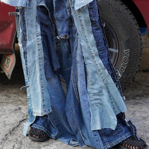 May include: A pair of blue denim jeans with multiple layers of fabric sewn together, creating a patchwork effect. The jeans are flared and have a distressed look.
