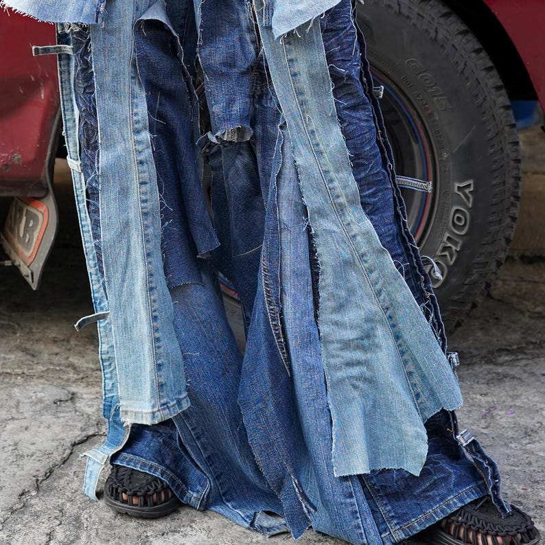 May include: A pair of blue denim jeans with multiple layers of fabric sewn together, creating a patchwork effect. The jeans are flared and have a distressed look.