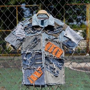 May include: A blue denim shirt with multiple patches of different shades of blue denim and orange fabric. The shirt has a button-up front and short sleeves. The denim patches are frayed and distressed, giving the shirt a vintage look.
