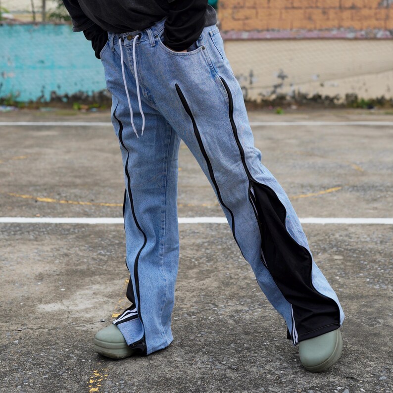 May include: Light blue denim jeans with black accents running along the seams and down the sides. The jeans have a drawstring waist and a relaxed fit. The design incorporates black fabric panels on the sides, creating a unique visual effect.