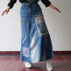 May include: A long denim skirt with multiple layers and patches. The skirt is made of blue denim and has a variety of different patches sewn onto it. The skirt is worn by a person with white sneakers.