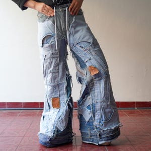 May include: Light blue denim pants constructed from multiple denim pieces, featuring a patchwork design with distressed details. The pants have a drawstring waist and multiple pockets, showcasing a unique, deconstructed aesthetic. The pants are a bold fashion statement.