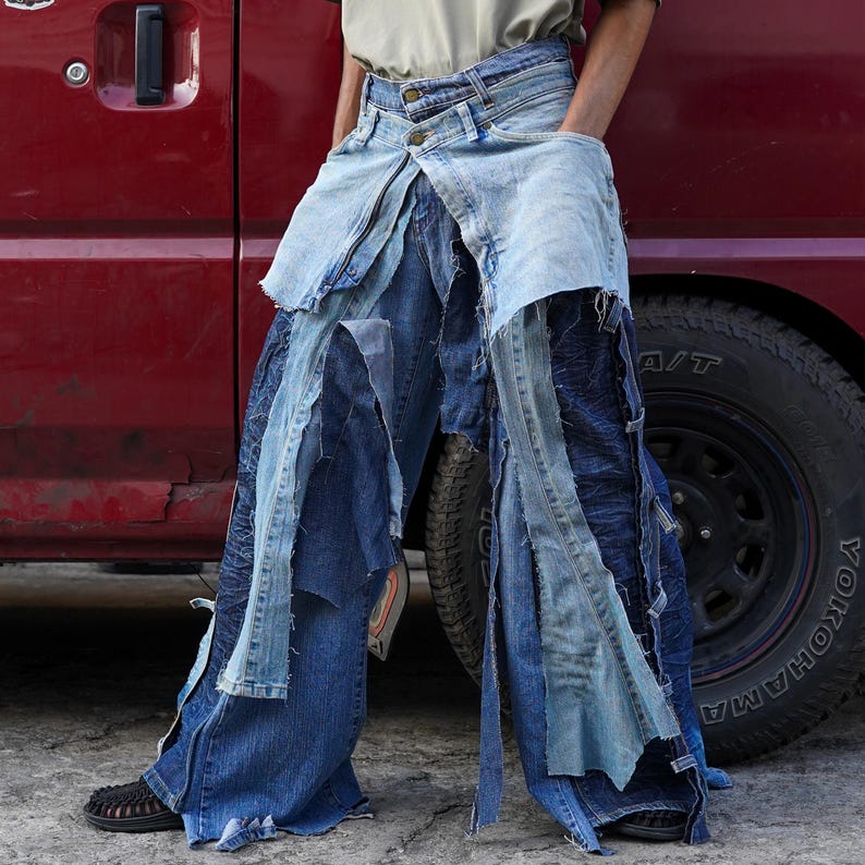 May include: A pair of blue denim jeans with multiple layers of fabric sewn together, creating a unique and layered look. The jeans are distressed and have a frayed hem.