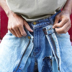 May include: A pair of blue denim jeans with a zipper detail and a frayed hem. The jeans are distressed and have a vintage look.
