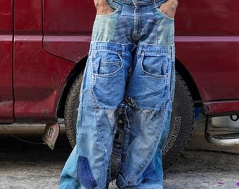 Pode incluir: Uma pessoa vestindo jeans azul feitos de várias camadas de denim, com costuras e remendos visíveis. O jeans é muito largo e tem um caimento relaxado.