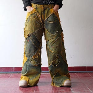 Op de afbeelding: Geel en groene patchwork jeans met meerdere zakken en distressed details. De jeans heeft een wijde pijpen en een uniek, artistiek design. De jeans wordt gedragen met witte sneakers.
